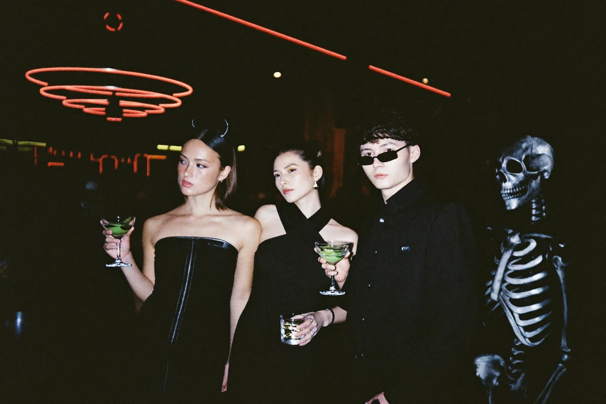 Stylish young adults in minimalist Halloween costumes holding cocktails at a neon-lit nightclub bar crawl