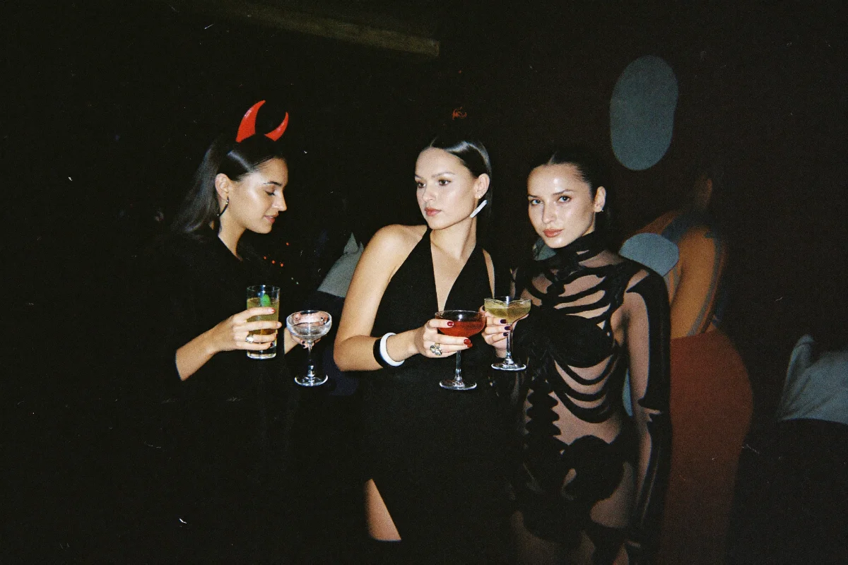 Young adults in Halloween costumes clinking cocktails at a bar crawl speakeasy