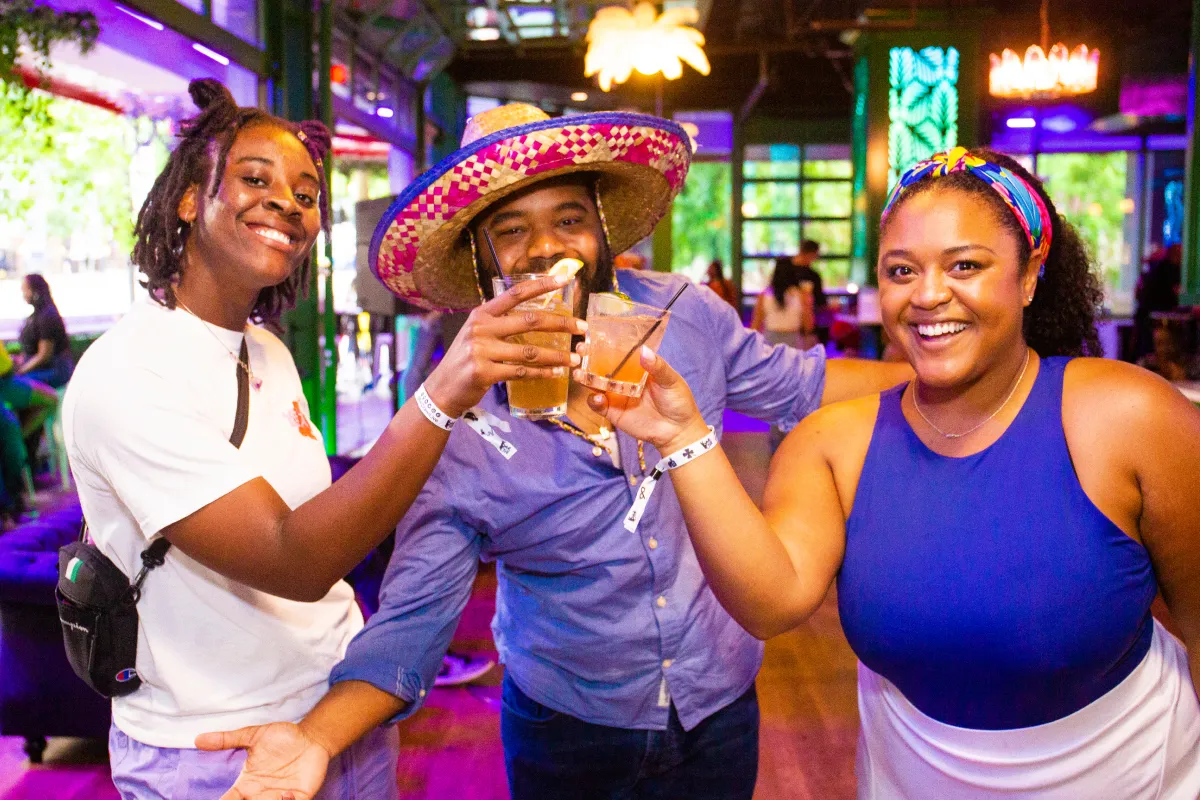 Man Wearing Sombrero While Two Females Toast Each Other During Cinco De Mayo Bar Crawl