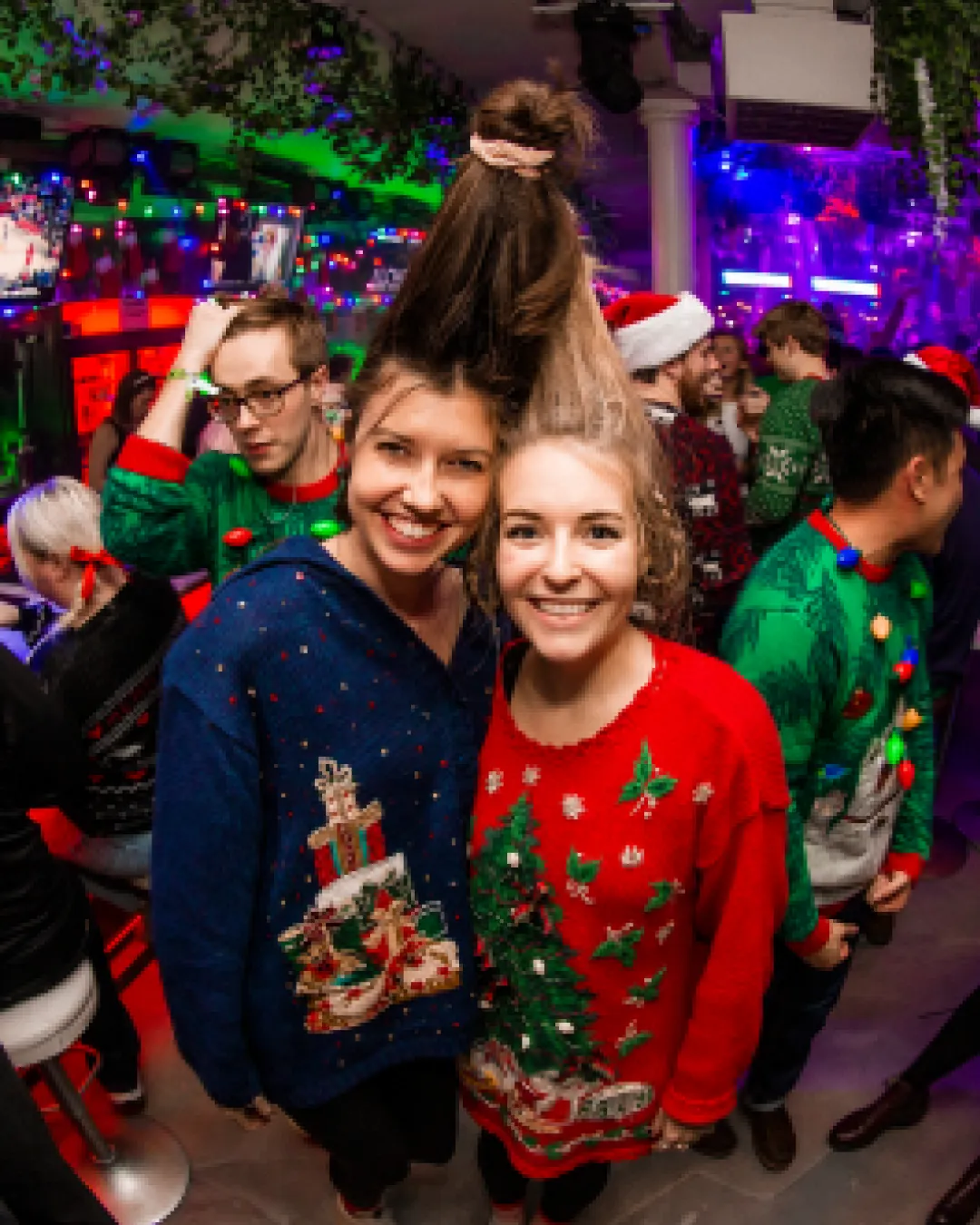Joyful and festive friends in funky Christmas sweaters laughing at bar crawl event
