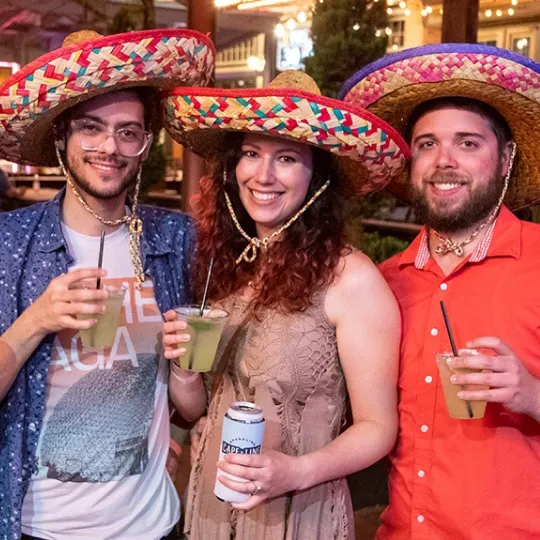 Group of three friends having a blast at the cinco de mayo bar crawl wearing sombrero hats with margaritas in hand