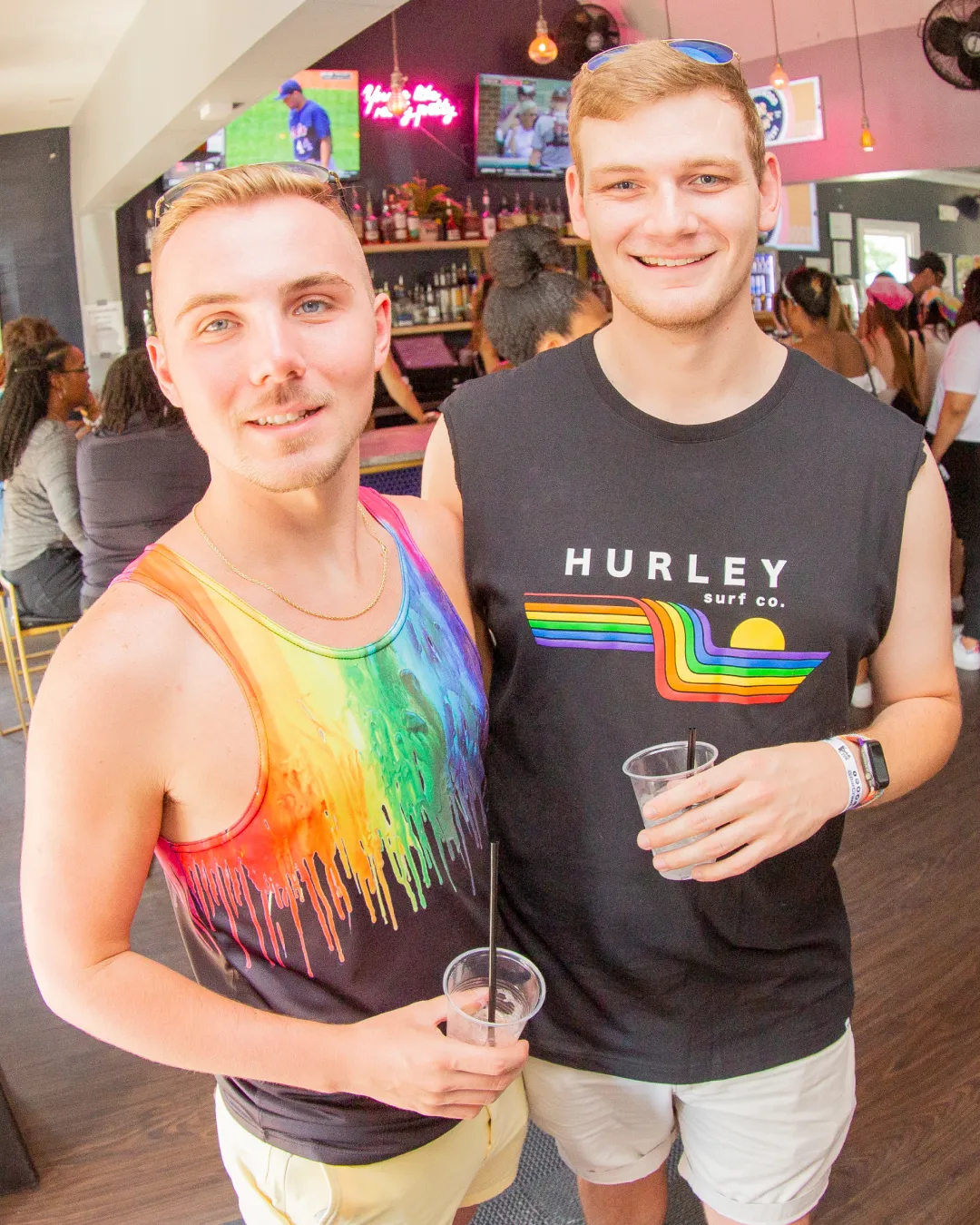 2 young individuals sip and smile while enjoying the atmosphere of the Pride Bar Crawl