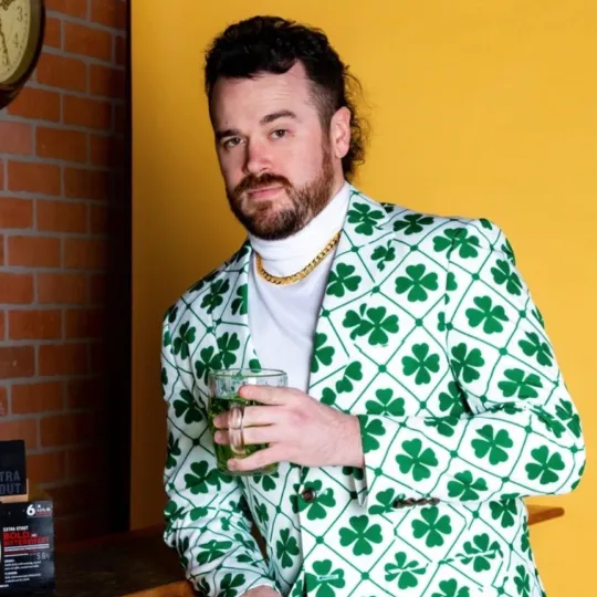 A man in a shamrock suit drinking green beer on St Patricks Day