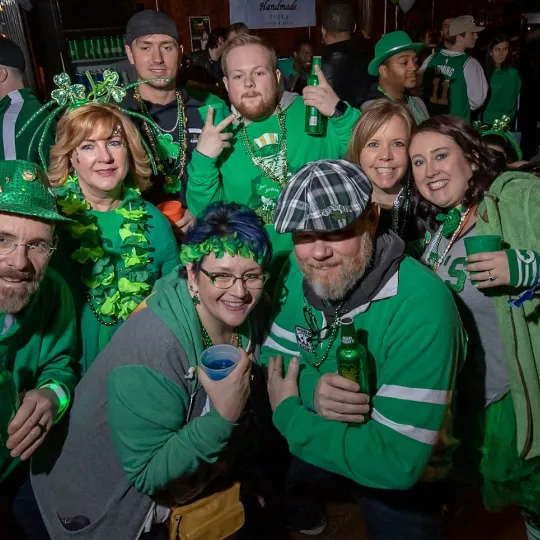 Giggles and cheers abound as friends, adorned with leprechaun beards and shamrock attire, make their festive mark on the bar scene during the St Patricks Bar Crawl