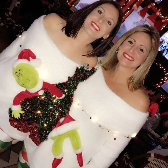 2 friends wearing coordinating ugly christmas sweaters that has the Grinch on it during the ugly christmas sweater bar crawl