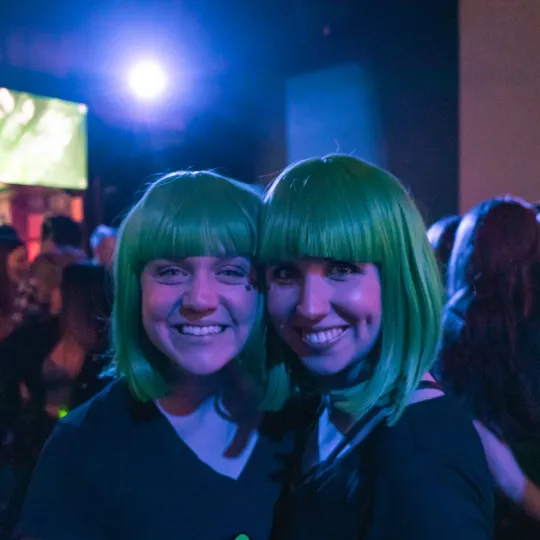 2 Girls wearing wigs pose playfully as they soak in the energetic vibes of the nightclub during the st paddys day bar crawl