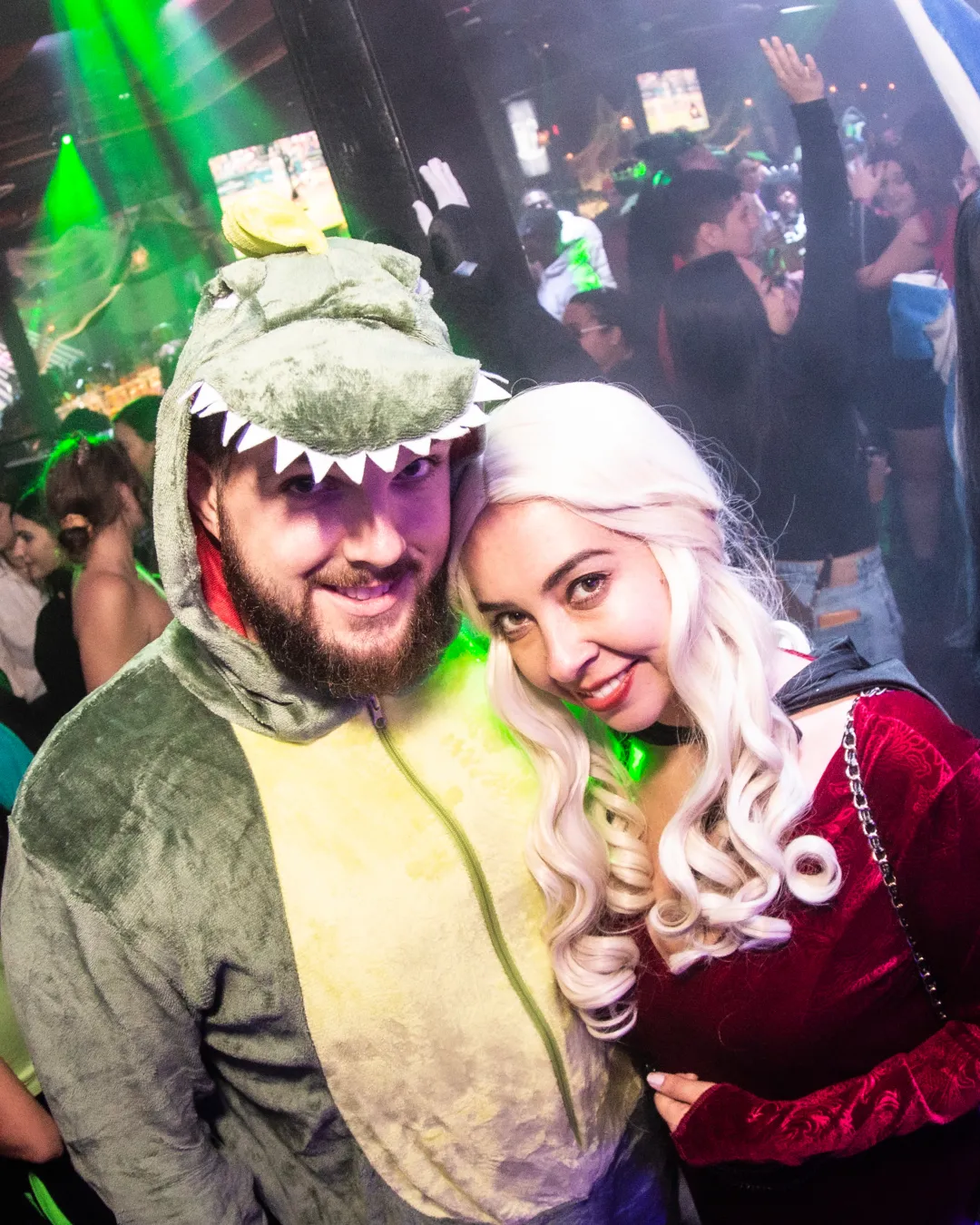A motley crew of two dressed in creative costumes embodying the iconic Khaleesi and her dragon from The Game Of Thrones tv series amid the Halloween bar crawl crowd
