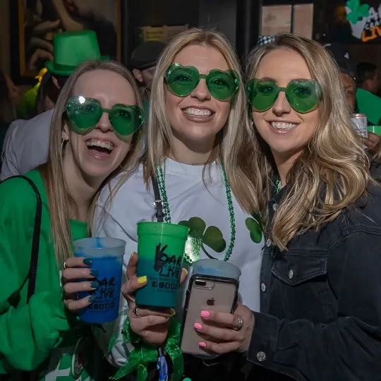 Exuberant friends, draped in green from head to toe and wearing green trendy glasses, forming the heart and soul of the St. Patrick's Day bar festivities
