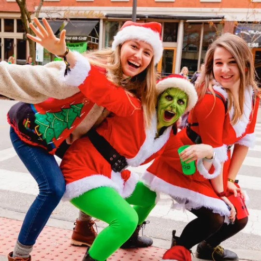 An enthusiastic trio of friends, all donned in christmas garb, making their way from one bar to the next during the christmas bar crawl in Cleveland
