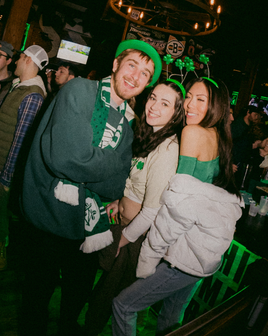A guy in a irish scarf and two cirls with shamrock head bands pose a picture in downtown cleveland
