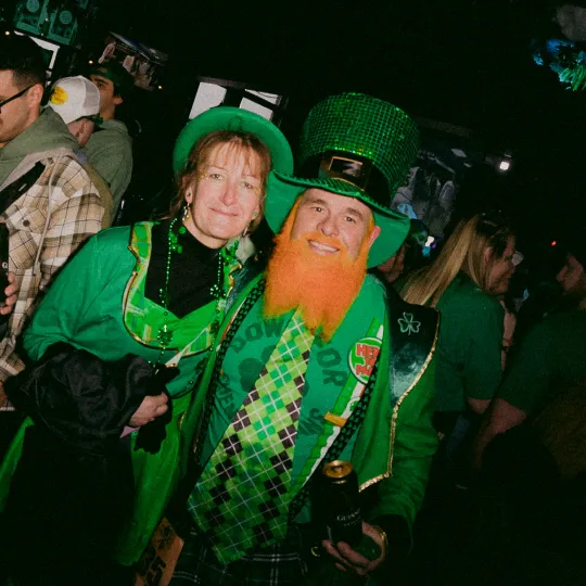 Elated friends in matching green and gold, standing out in the crowd as they revel in the joyous spirit of the St. Patrick's Day bar event.
