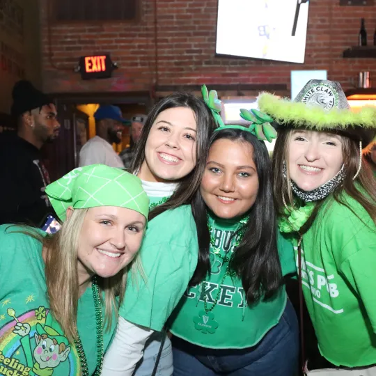 Magnetic group, drawing attention with their playful green tutus and shamrock bandanas, reveling in the heart of the St. Patrick's Day bar event
