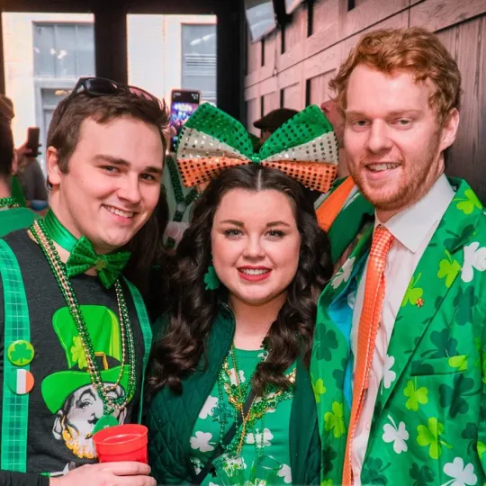 Vivacious crew in green hats and irish flags, setting the gold standard for festive fun at the St. Patrick's Day bar event.