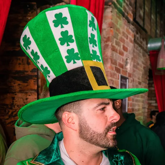 Young male trendsetter in a unique and eye-catching gigantic green hat setting the style standard for the St Patricks Bar Crawl in Detroit
