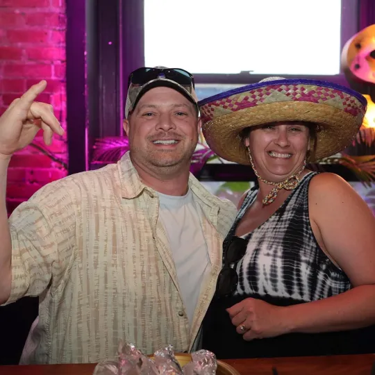 Smiling faces peeking out from beneath grand sombreros, a a happy could fully immerse in the bar crawl's festive spirit while getting ready for the taco eating contest at the Tacos and Tequila bar crawl
