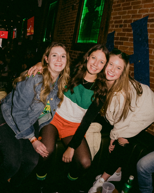 A girl in an irish flag dress takes a picture iwth her friends durng a st patricks day pub crawl in hoboken
