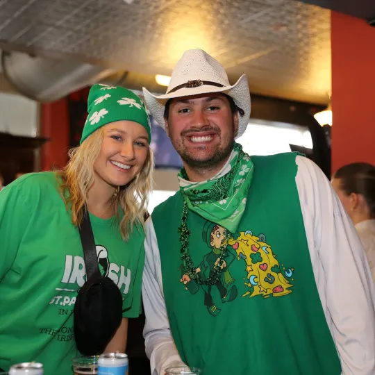 A girl and a guy in a cowboy hat wearing a tshirt with the lucky charms leprauchan smiling during the St Pats Bar Crawl in Hoboken.