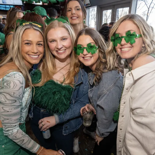 Jubilant young woman in festive attire, exchanging stories, drinks, and memories against the backdrop of the lively St. Patrick's Day bar crawl in Hoboken
