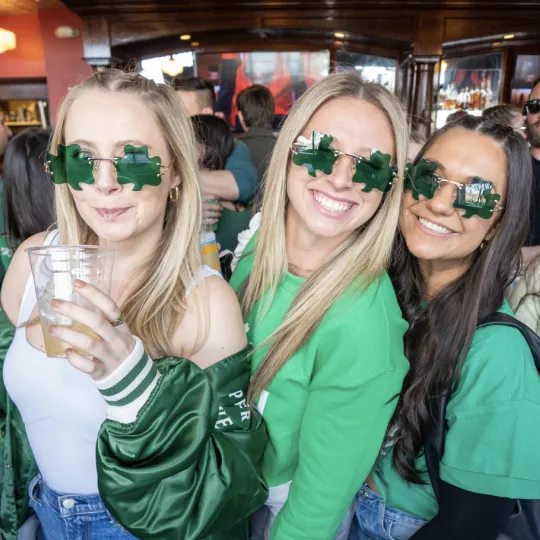 Friends, united in their green shamrock glasses, creating a symphony of laughter and dance amidst the St. Patrick's Day bar revelry
