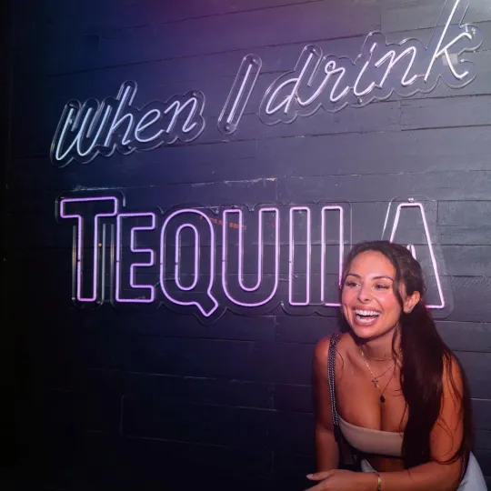 Girl standing and laughing in front of a sign that says "When I drink Tequila" at Fat Taco in Hoboken