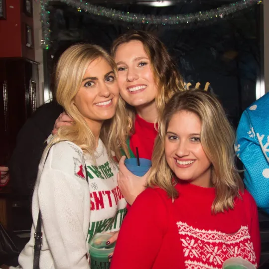 Cheerful and merry girlfriends happily celebrating at the ugly sweater bar crawl in Philadelphia rocking their ugliest sweaters
