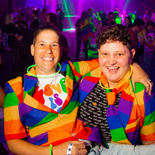 2 individuals in rainbow suits smiling bigger than ever at the Pride Bar Crawl