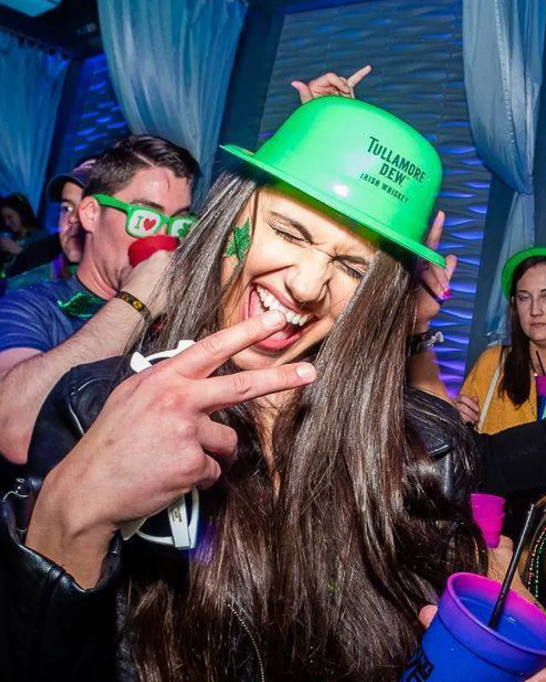 A charismatic and magnetic girl stands out in a green bucket hat soaking in the nightclub's electric atmosphere from the VIP lounge at the st patricks bar crawl
