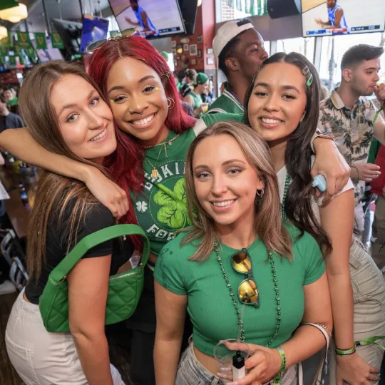 Lively gal pals, draped in festive green and sprinkled with gold, embodying the joyous essence of the St. Patrick's Day bar crawl in Philly
