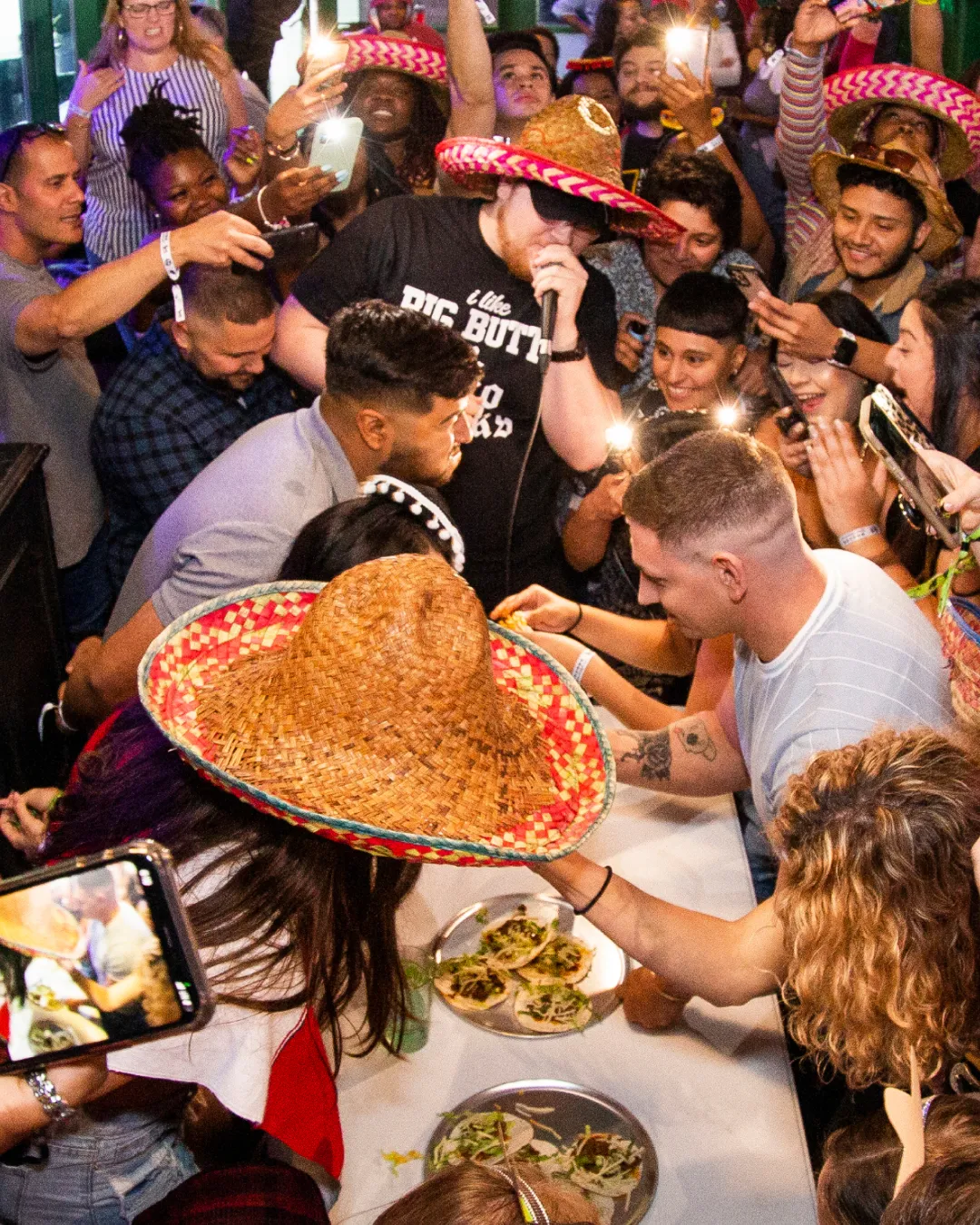 Vivacious people in sombreros gathered around a table with fierce devotion to the taco eating contest  capturing the heart and soul of the Tacos and Tequila-themed night
