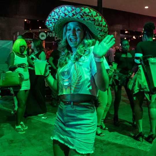 Young club goer in a striking sombrero ensemble, radiating confidence as they pose against the backdrop of the club's iconic dance floor during the tacos and tequila bar crawl