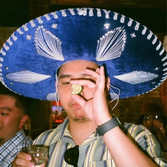 Guy holding up a lime ready to take a tequila shot wearing a sombrero hat for the cinco de mayo bar crawl