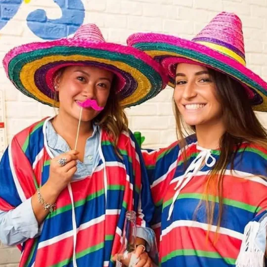 Bubbly girls in colorful sombreros and ponchos, sharing laughs and memories at the lively Tacos and Tequila bar event 
