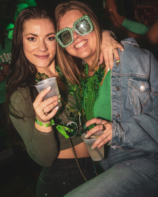 2 girls hug and cheers their irish drinks during a st patricks day bar crawl in raleigh
