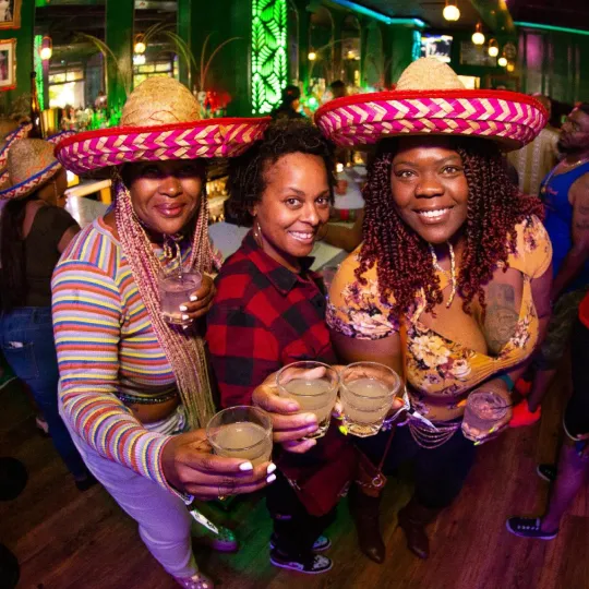 3 girls cheersing their Margaritas wearing sombrero hats during the tacos and tequila bar crawl in Raleigh