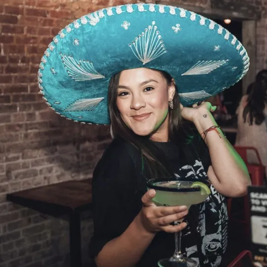 Stunning girl in a sombrero hat eflecting the club's neon ambiance, enjoying a margarita at the bar during the tacos and tequila bar crawl