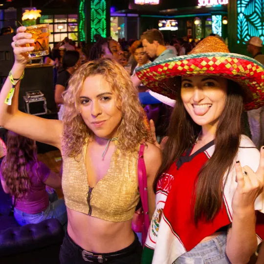 Girlfriends dressed to the nines in their most hispanic sombrero hats enjoying the electric ambiance of the city's hottest nightclub and raising a toast to tacos and tequila during the bar crawl