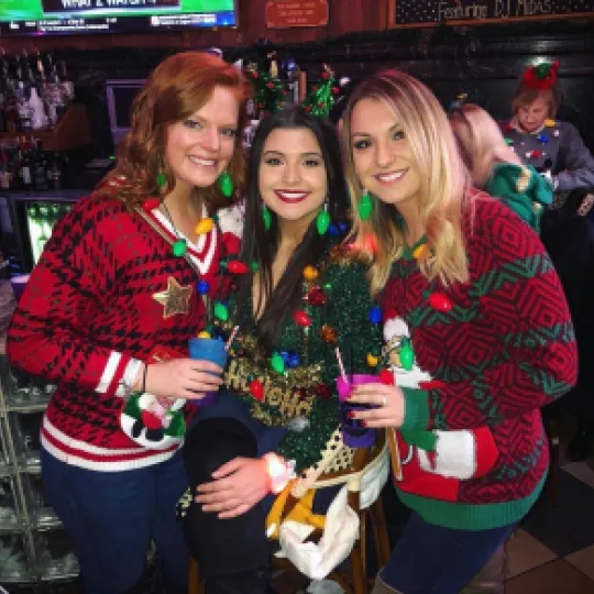 3 girls sitting at one of the best bars in Richmond rocking their christmas light necklaces and in their ugliest sweaters during the holiday bar crawl