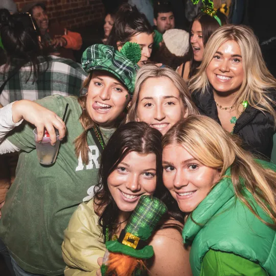 Beaming faces of young trendy women beneath green hats in a circle of friends basks in the vibrant ambiance of the bar crawl's Irish celebration at the st paddys day bar event
