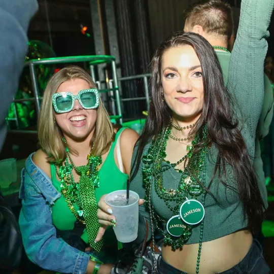 Friends, united in their green-glittered outfits, creating a symphony of laughter and dance amidst the St. Patrick's Day bar revelry
