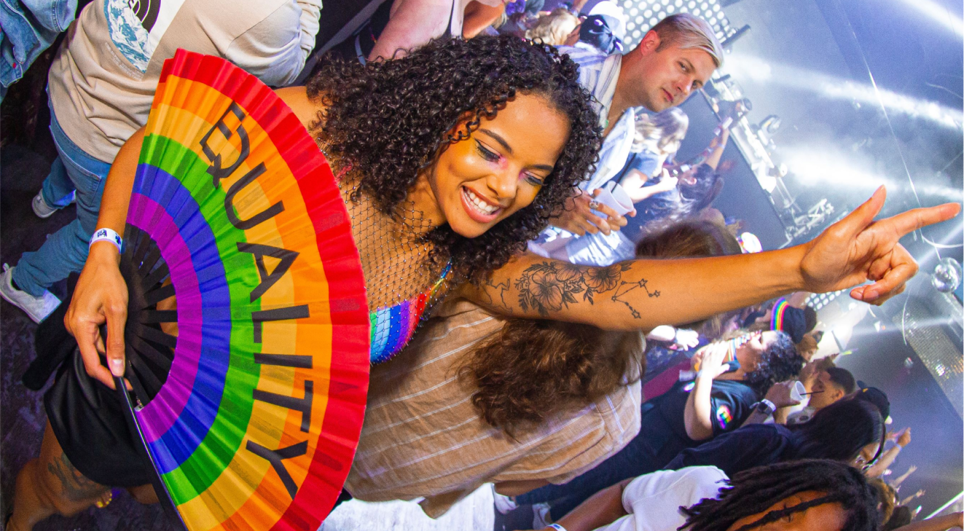 a group of people dressed in rainbow colors at the pride bar crawl and a girl holding an equality fan