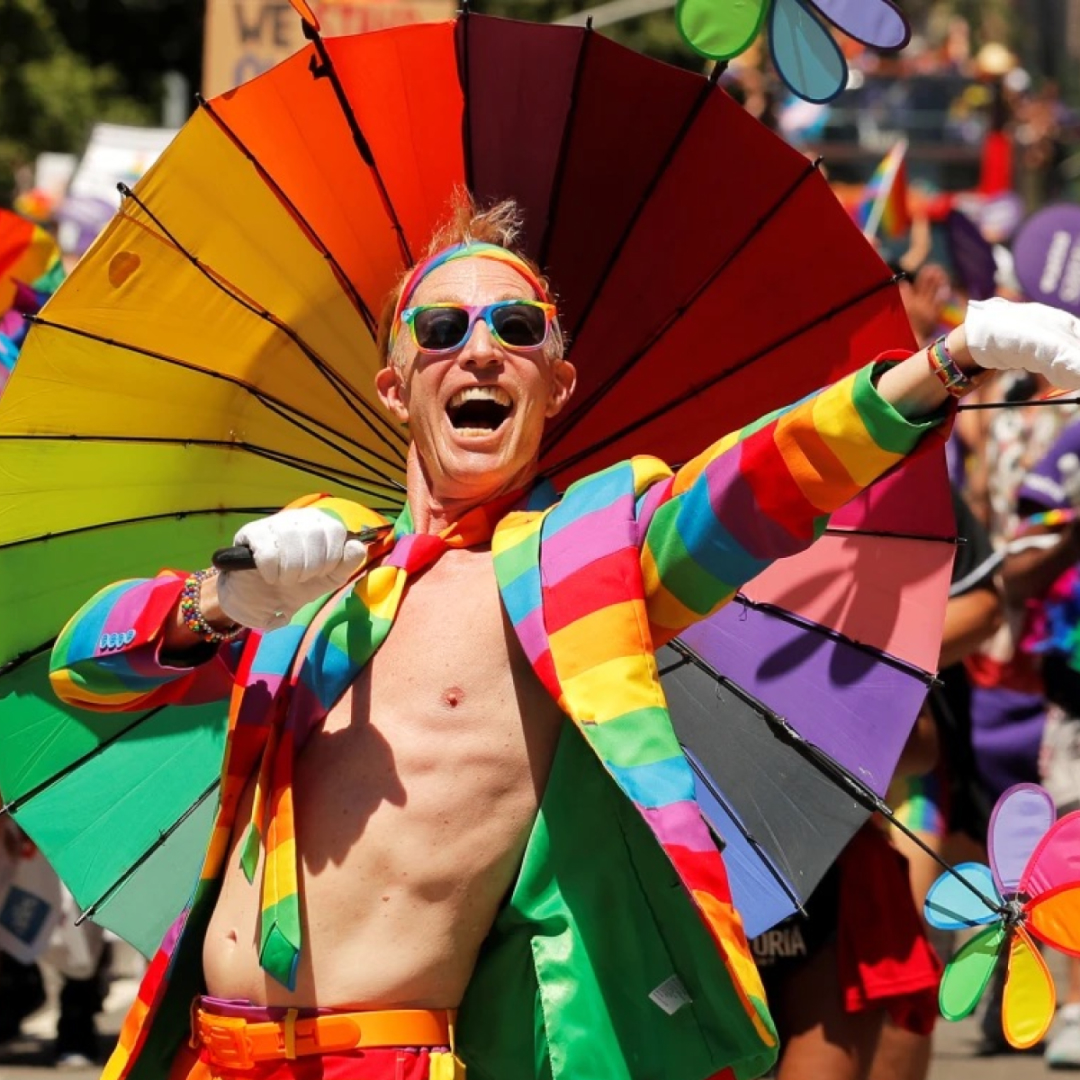 A man wearing a rainbow colored blazer and holding a rainbow colored flag celebrating pride