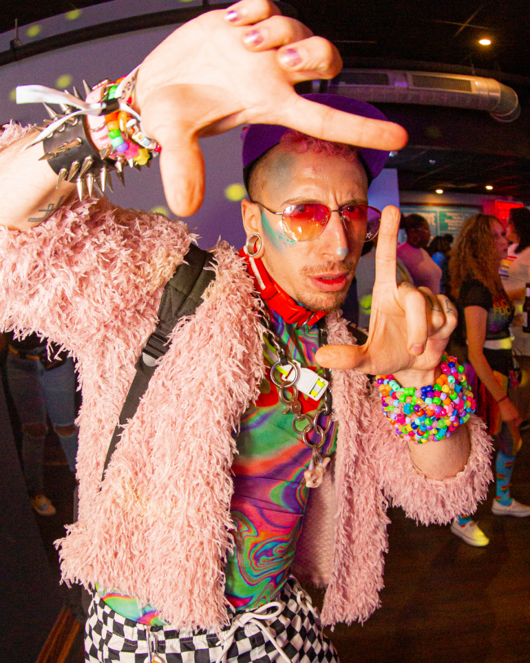 Man dressed up in rainbow colored clothing for Philadelphia Pride Bar Crawl making a square with his hands representing a camera