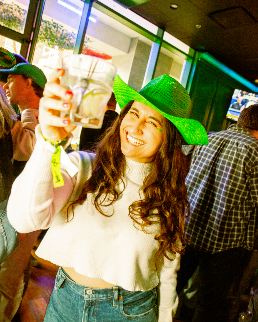 Girl in green cowboy hat celebrating St. Patrick's Day at a Bar Crawl in Raleigh cheersing her drink towards the camera